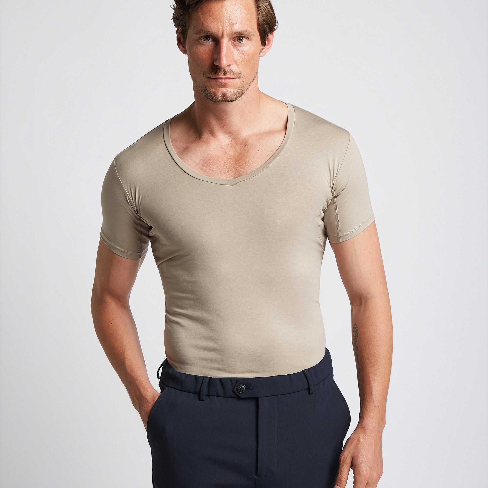 A man wearing a khaki-colored V-neck undershirt with short sleeves, paired with dark trousers.